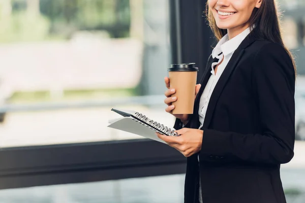 Cropped shot of smiling businesswoman with coffee to go and notebook in conference hall — Stock Photo