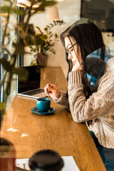 Seitenansicht der schönen brünetten Frau in Gläsern sitzt im Café mit einer Tasse Tee — Stockfoto