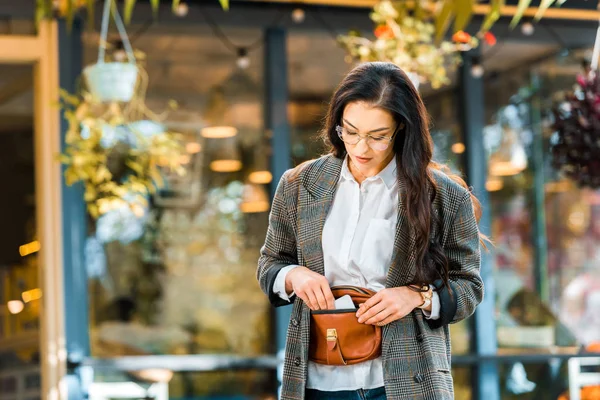 Schöne Frau im Herbst-Outfit nimmt etwas aus Handtasche auf der Straße in der Nähe von Café — Stockfoto