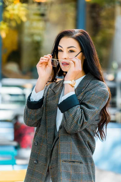 Schöne Frau in Jacke trägt eine Brille auf der Straße in der Nähe eines Cafés und schaut weg — Stockfoto