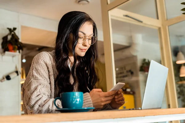 Oberflächenebene einer schönen Frau, die mit Laptop im Café sitzt und das Smartphone benutzt — Stockfoto