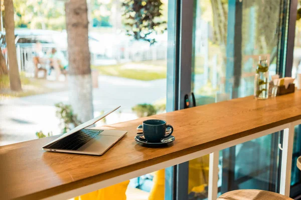 Laptop and cup of coffee on wooden cafe counter — Stock Photo