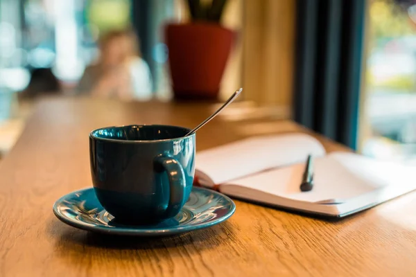 Taza de café con cuchara y cuaderno abierto con pluma en la mesa de madera en la cafetería - foto de stock