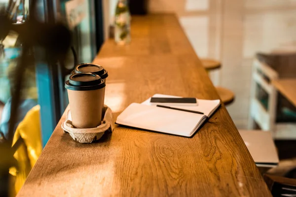 Deux tasses à café jetables, bloc-notes ouvert avec stylo sur le comptoir du café — Photo de stock