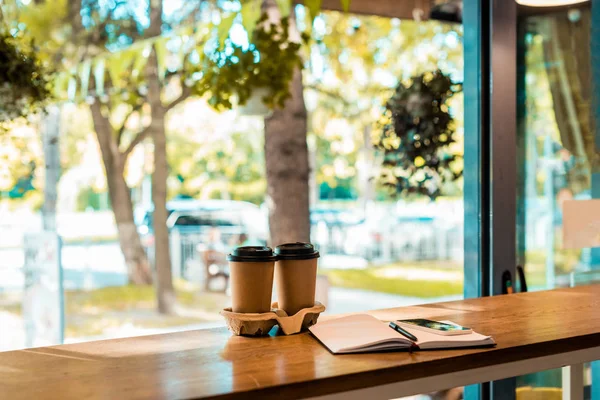 Zwei Kaffee in Pappbechern, geöffnetes Notizbuch mit Stift auf der Cafétheke — Stockfoto