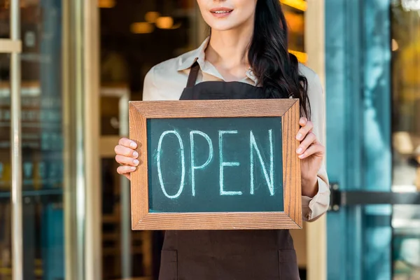 Cropped image of cafe owner in apron holding open signboard near cafe — Stock Photo