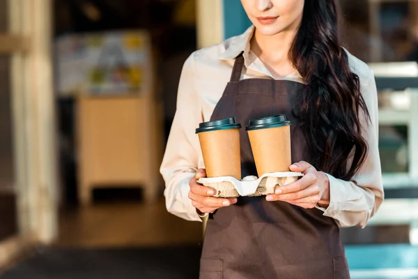 Cropped image of waitress in apron holding two disposable coffee cups near cafe — Stock Photo