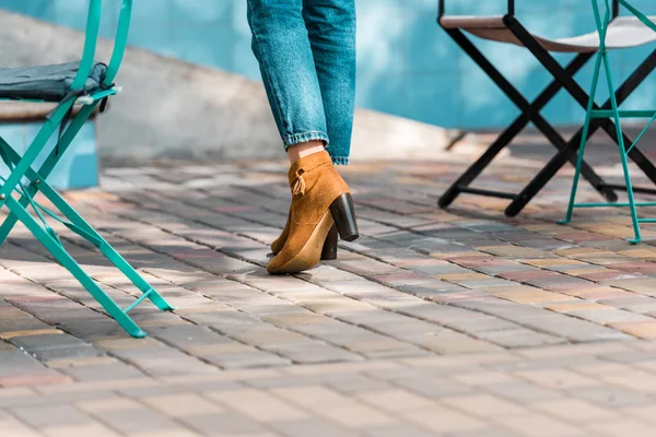 Low section of woman in jeans high heels standing on street near cafe chairs — Stock Photo