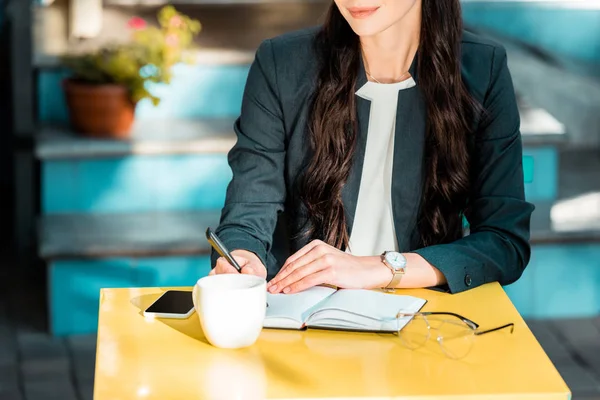 Abgeschnittenes Bild einer Geschäftsfrau, die im Straßencafé etwas zu Notizbuch schreibt — Stockfoto