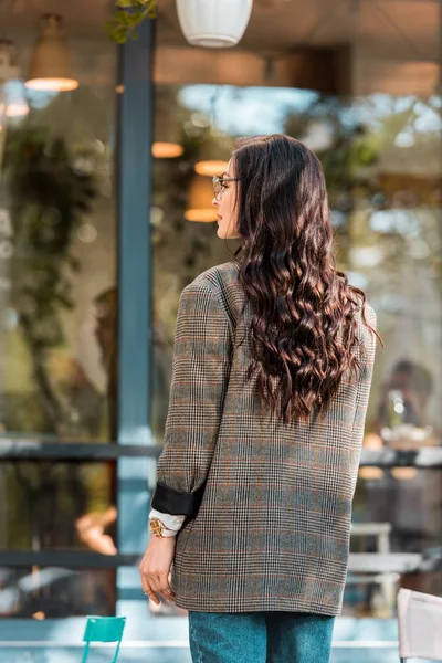 Rückansicht einer schönen Frau im Herbst-Outfit, die auf der Straße in der Nähe eines Cafés steht — Stockfoto
