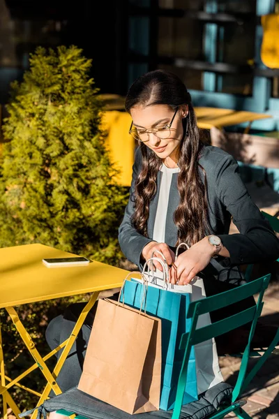 Красивая женщина сидит за столом в уличном кафе и смотрит в сумку — стоковое фото