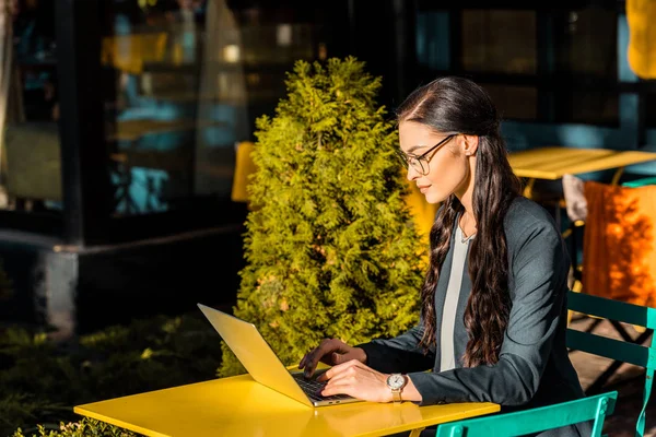 Brunette concentrée femme d'affaires travaillant avec ordinateur portable sur la terrasse du restaurant — Photo de stock