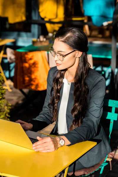 Attractive young businesswoman working with laptop on restaurant terrace — Stock Photo