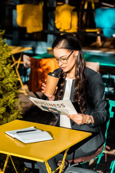 Mulher atraente segurando café para ir e ler jornal de negócios enquanto sentado no terraço do café — Fotografia de Stock