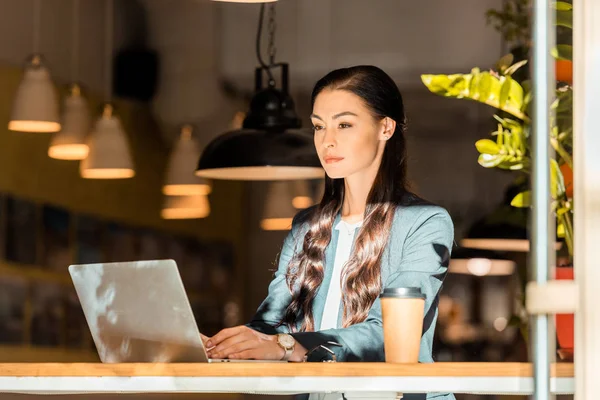 Attractive brunette freelancer working with laptop at coffee shop — Stock Photo