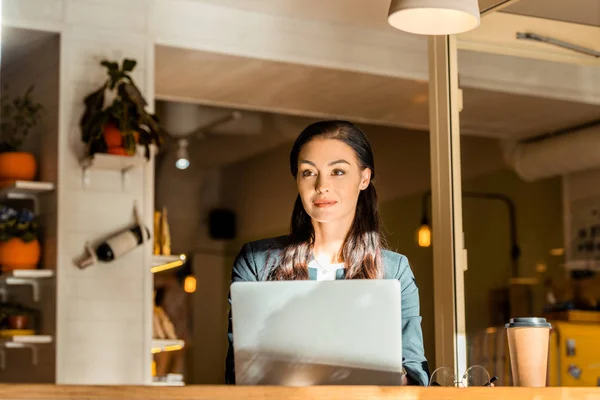 Hermosa freelancer femenina que trabaja con el ordenador portátil en la cafetería con taza de café - foto de stock