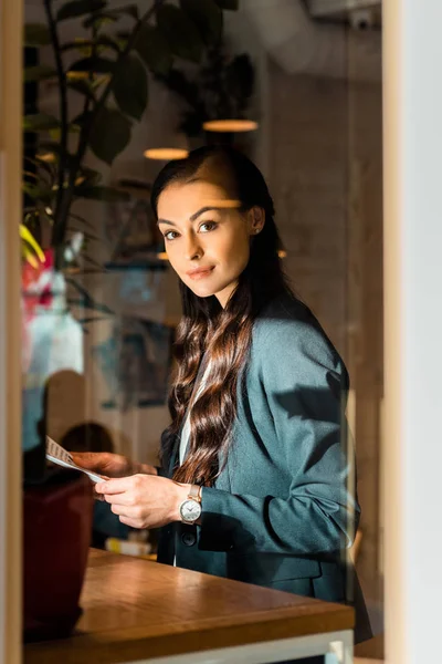 Attrayant brunette femme d'affaires en veste noire tenant journal au café — Photo de stock