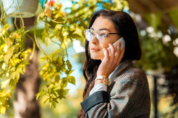 Hermosa mujer con estilo en gafas de vista hablando en el teléfono inteligente - foto de stock