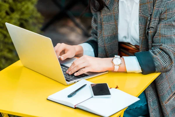 Vista parcial del freelancer de negocios trabajando con laptop en la terraza del restaurante con diario y smartphone — Stock Photo