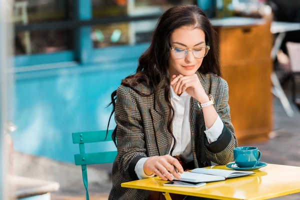 Beautiful freelancer working on restaurant terrace with planner, smartphone and cup of coffee — Stock Photo