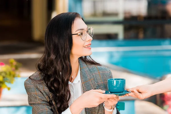 Attractive woman taking coffee cup from waitress on restaurant terrace — Stock Photo
