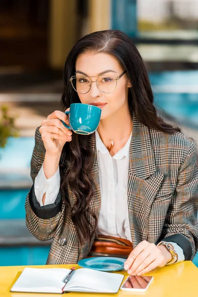 Attraktive Frau trinkt Kaffee auf Restaurantterrasse mit Planer und Smartphone — Stockfoto