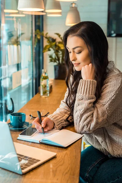 Attrayant freelance femme travaillant avec planificateur, smartphone et ordinateur portable dans un café — Photo de stock