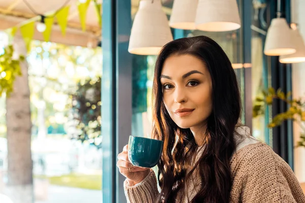 Beautiful woman in autumn sweater holding cup of coffee in cafe — Stock Photo