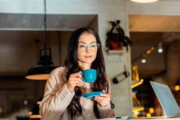 Atractiva mujer bebiendo café en el descanso en la cafetería con el ordenador portátil - foto de stock