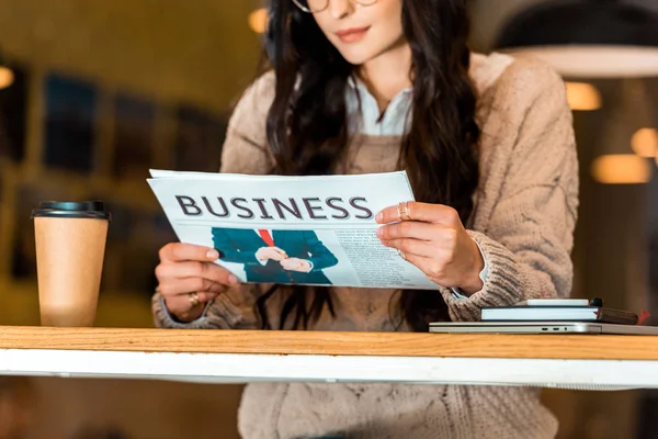 Vista cortada de mulher lendo jornal de negócios no café com café para ir — Fotografia de Stock