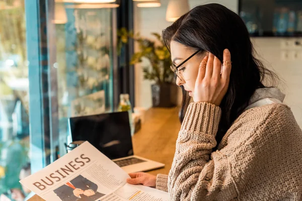 Приваблива жінка читає бізнес-газета в кафе з ноутбуком — стокове фото