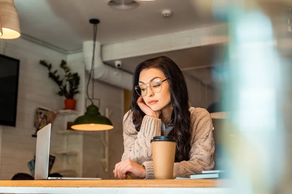 Attraente freelance annoiato che lavora su computer portatile con caffè per andare in caffè — Stock Photo