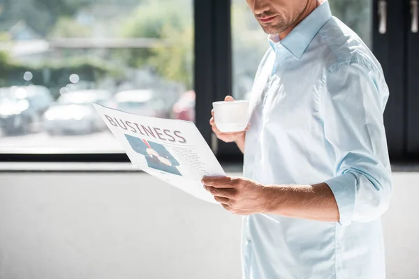 Tiro recortado de empresário adulto bonito na camisa beber café e ler jornal — Fotografia de Stock