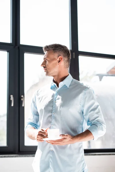 Thoughtful adult man with cup of coffee looking at window — Stock Photo