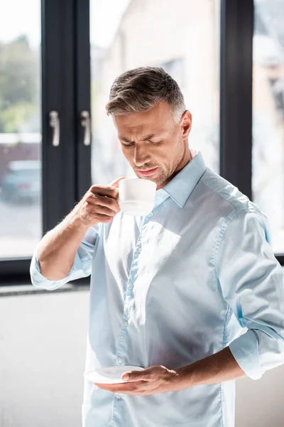 Hombre adulto serio beber café frente a la ventana - foto de stock