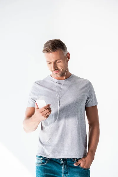 Attractive adult man in blank grey t-shirt listening music with smartphone and earphones isolated on white — Stock Photo