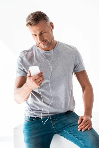 Bell'uomo adulto in t-shirt bianca grigia che ascolta musica con smartphone e auricolari isolati su bianco — Foto stock