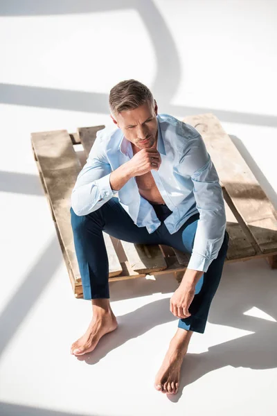 Vue grand angle de bel homme adulte assis sur une palette en bois sur blanc — Photo de stock