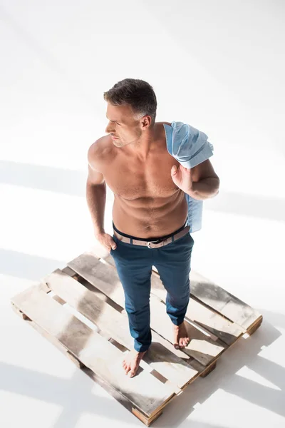 High angle view of shirtless sexy adult man standing on pallet on white — Stock Photo