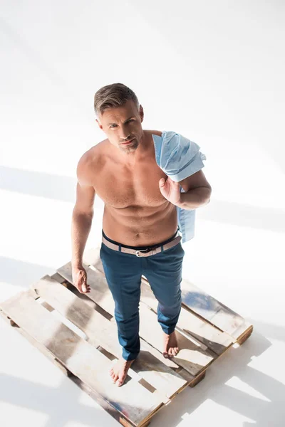 High angle view of shirtless handsome adult man standing on pallet on white and looking at camera — Stock Photo