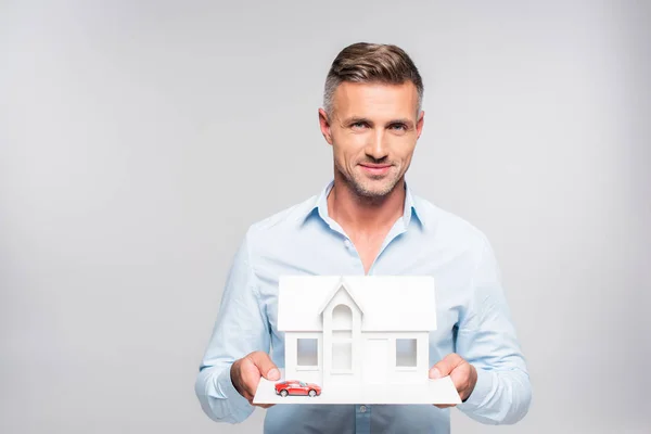 Handsome adult man holding paper model of house and toy car isolated on white — Stock Photo