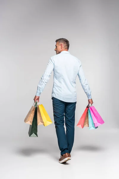 Vista trasera del hombre adulto llevando coloridas bolsas de compras en blanco - foto de stock