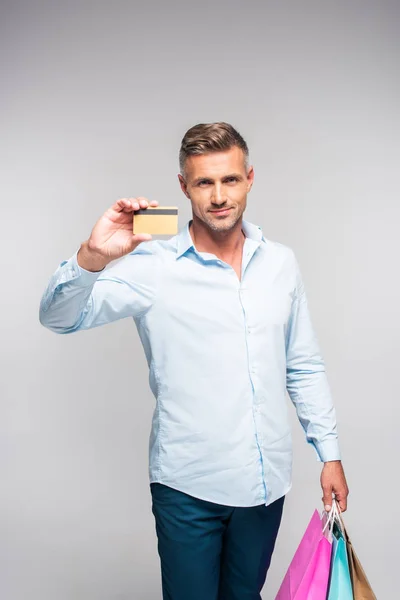 Handsome man holding shopping bags and credit card isolated on grey — Stock Photo