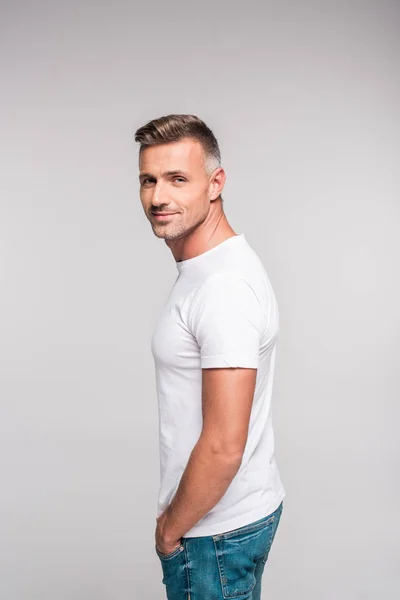 Seitenansicht eines gutaussehenden Mannes in weißem T-Shirt, der isoliert auf grau in die Kamera lächelt — Stockfoto