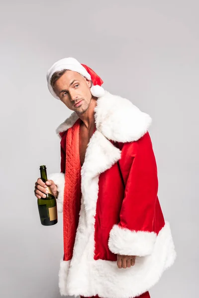 Handsome man in santa costume holding bottle of champagne and looking away isolated on grey — Stock Photo