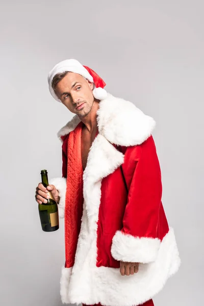 Hombre guapo en traje de santa celebración botella de champán y mirando hacia otro lado aislado en gris - foto de stock