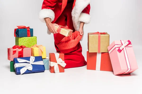 Cropped shot of santa claus packing gifts in red bag on grey — Stock Photo