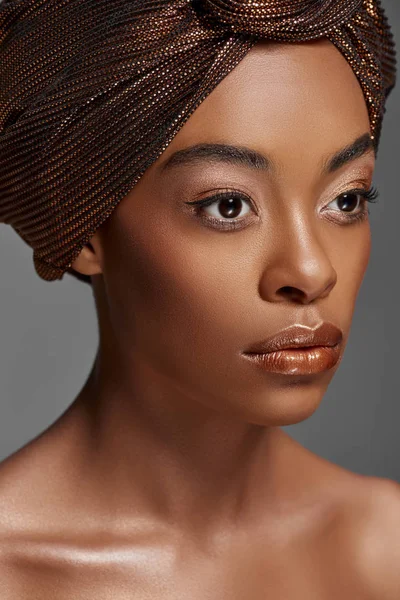 Портрет привлекательной африканской американки с обёрткой головы и голыми плечами, смотрящей в сторону изолированной на сером — стоковое фото