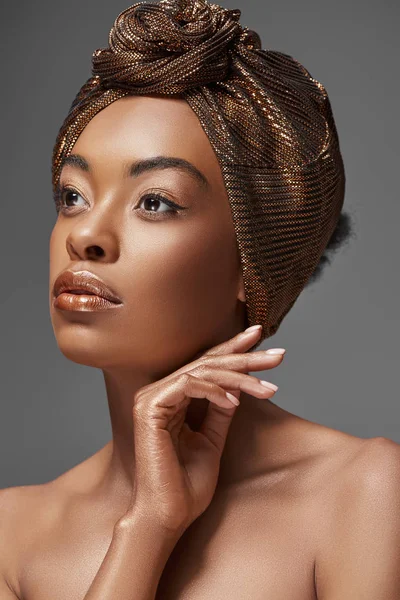 Retrato de mujer afroamericana con envoltura en la cabeza y hombros desnudos mirando hacia otro lado aislado en gris - foto de stock