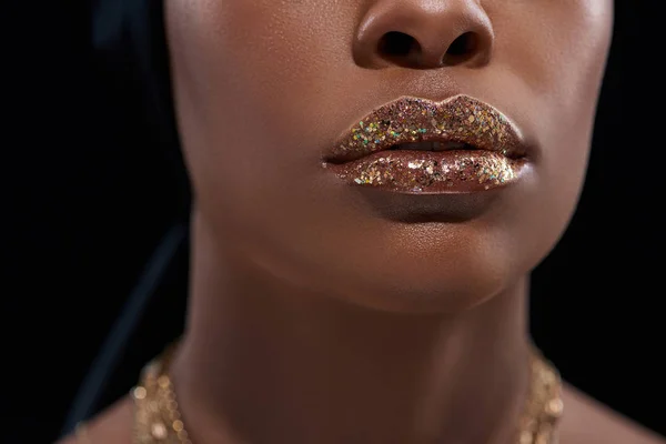 Cropped shot of african american woman with sparkling lip gloss isolated on black — Stock Photo